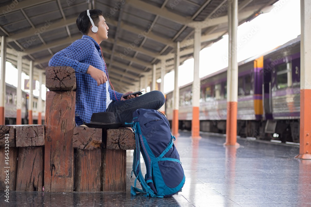 man traveler with backpacker listening to music at trainstation