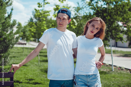 Young couple in white T-shirts standing in park. Mock up.