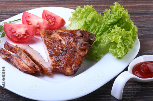 grilled pork chops with tomato, leaves lettuce and ketchup on plate.
