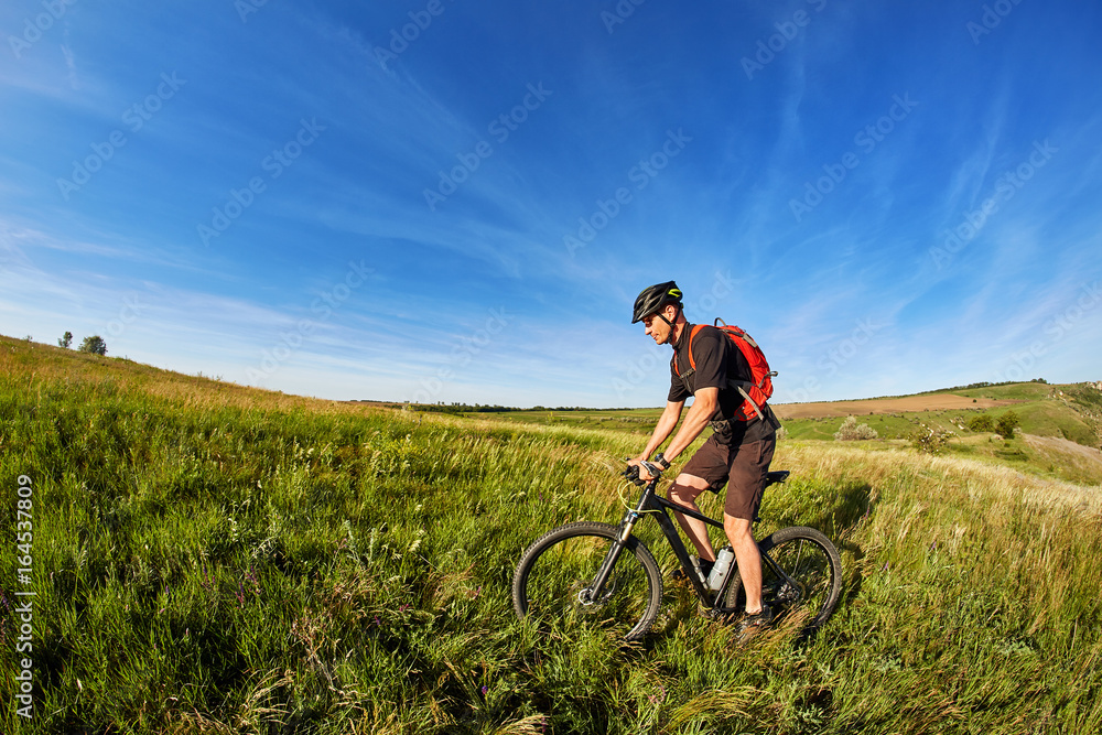 Young man riding on a bicycle on green meadow with a backpack Young man riding on a bicycle on green meadow with a backpack