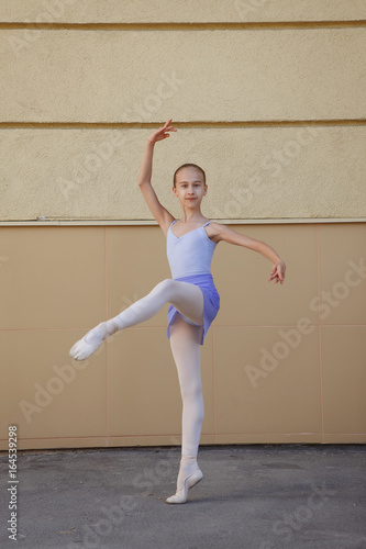 Ballet dancer dancing on street. Young ballerina on yellow background full length