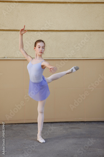 Ballet dancer dancing on street. Young ballerina on yellow background full length