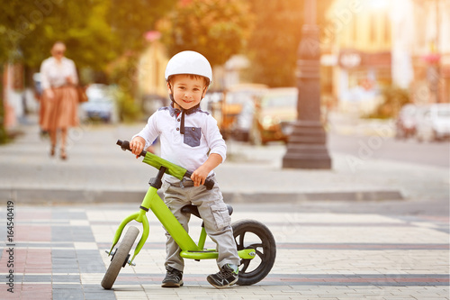 Fototapeta Naklejka Na Ścianę i Meble -  Little boy kid in helmet ride a bike in city park. Cheerful child outdoor.