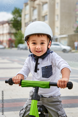 Little boy kid in helmet ride a bike in city park. Cheerful child outdoor.