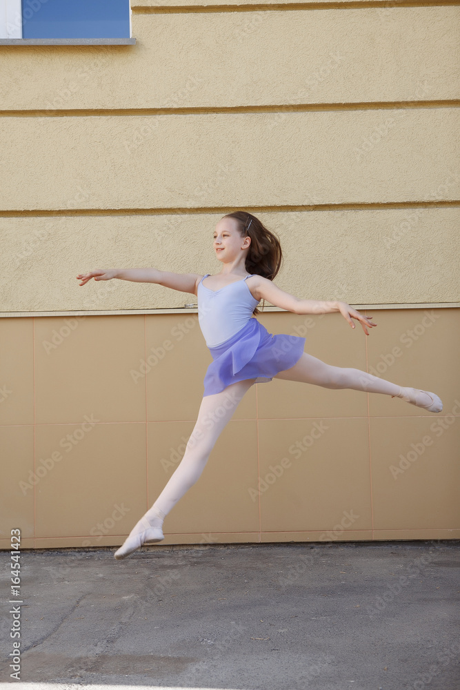 Ballet dancer dancing on street. Young ballerina jump on yellow background full length