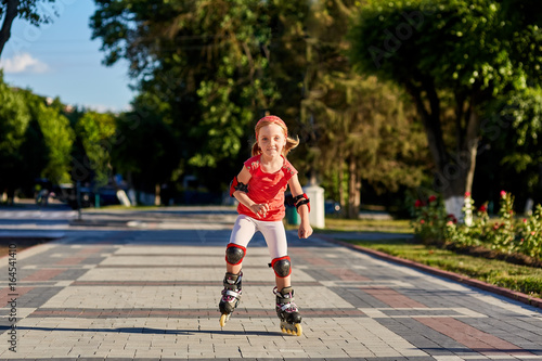 Girl riding on roller skates in skatepark summer outdoor. Child in a red suit for the rollers