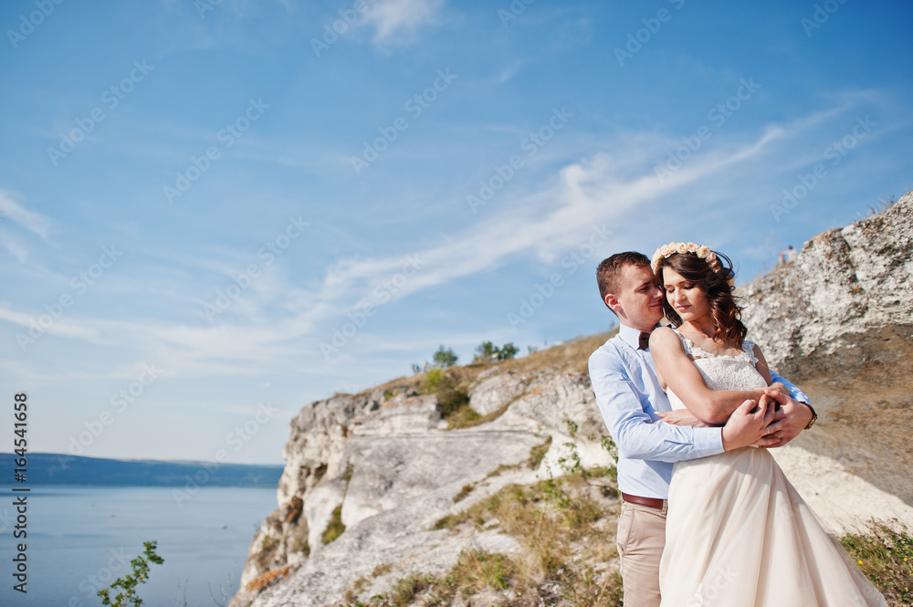 Gorgeous wedding couple posing next to the cave with breathtaking view of lake in the background.