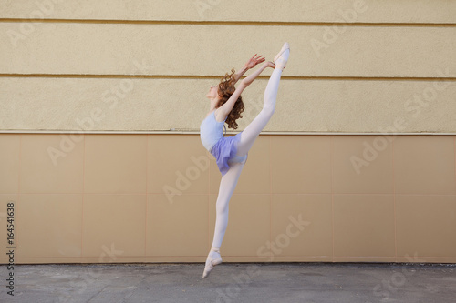 Ballet dancer dancing on street. Young ballerina jump on yellow background full length