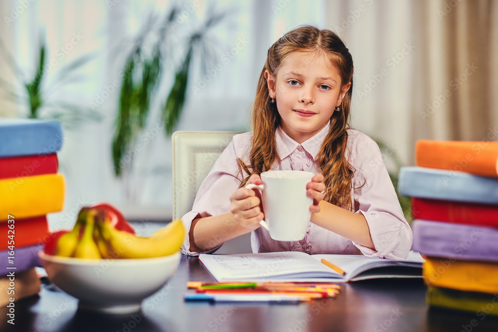 Positive little girl drinks morning tea before studying. Positive little girl drinks morning tea before studying.