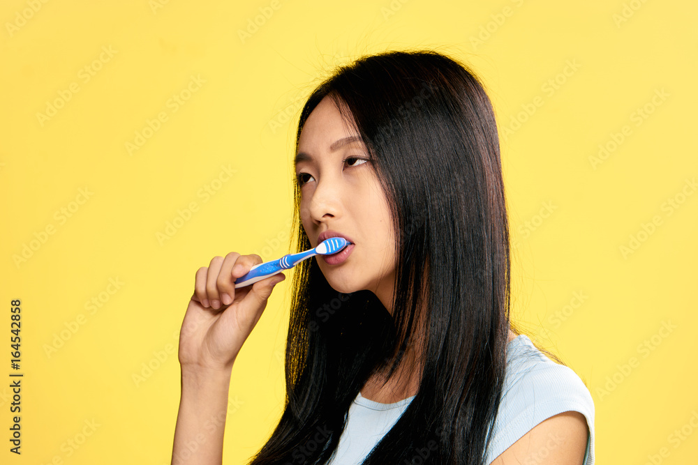 Beautiful young woman on a yellow background brushes teeth, portrait, asian Beautiful young woman on a yellow background brushes teeth, portrait, asian
