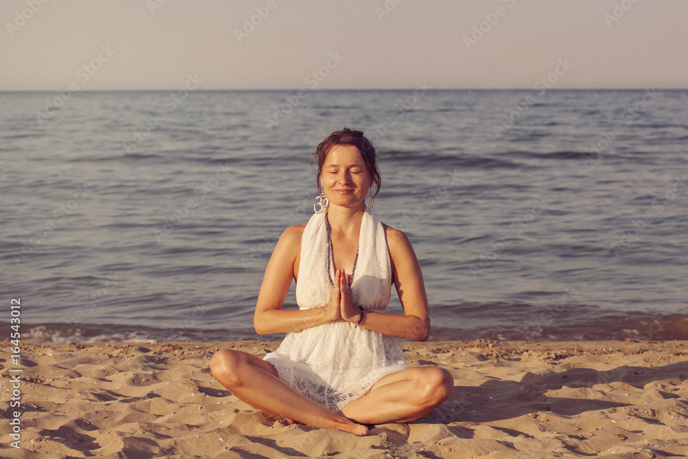 Young woman meditating by the seashore in sunset