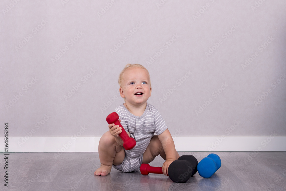 Cute smiling toddler lifting a dumbbell and lokking at camera Cute smiling toddler lifting a dumbbell and lokking at camera