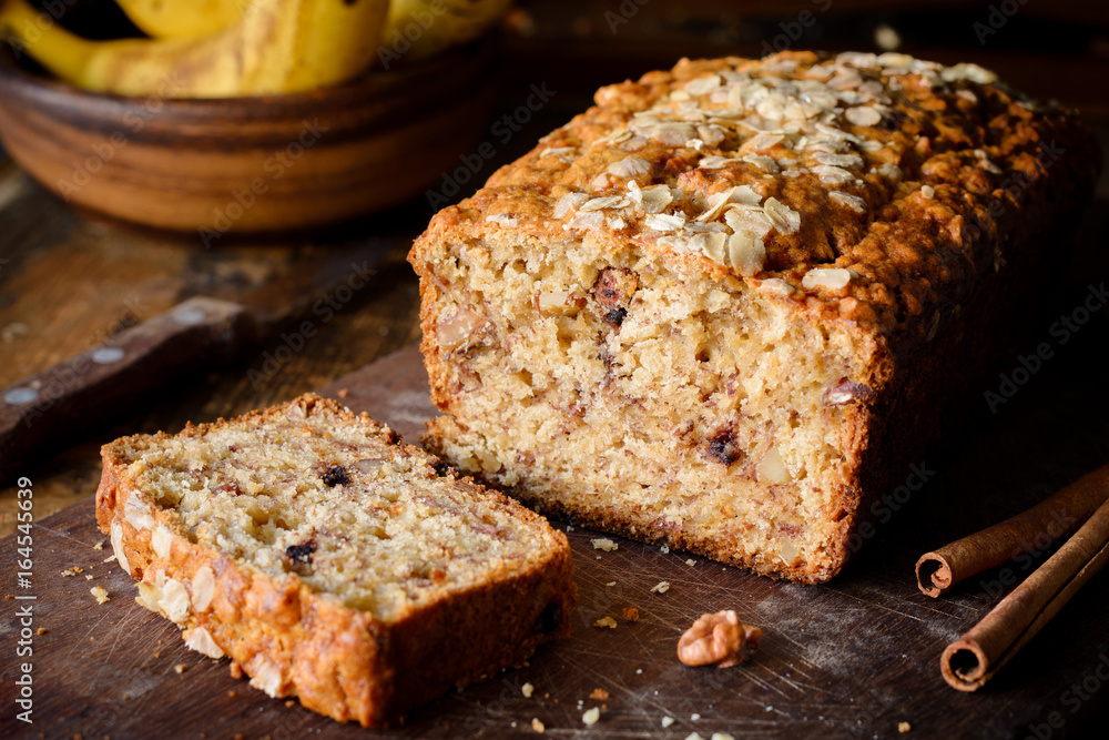 Banana bread loaf with walnuts and cinnamon on wooden board. Closeup view