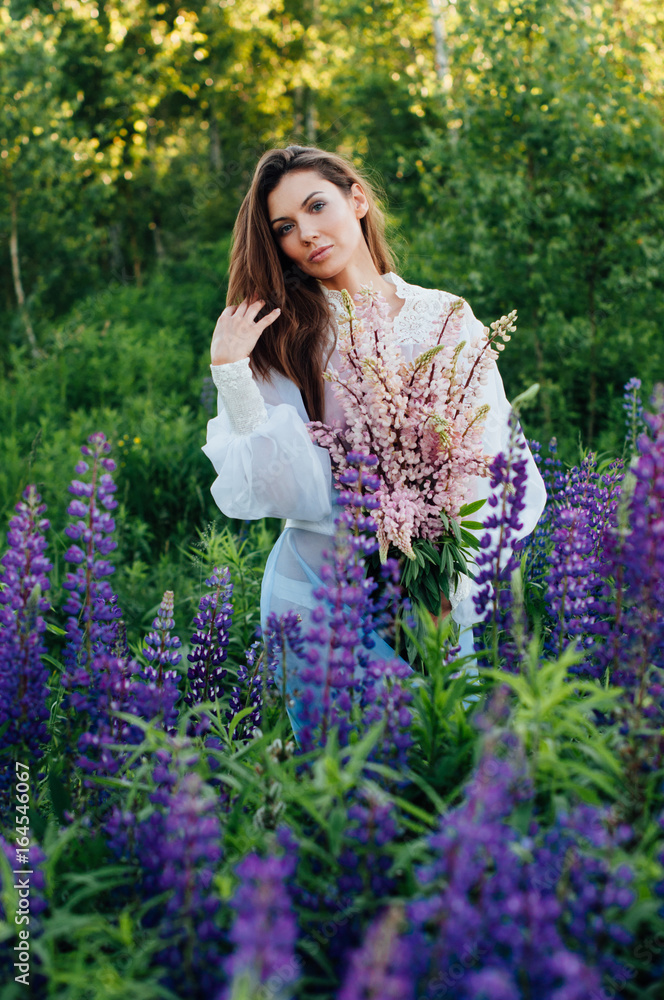 Beautiful woman dressed in a dress in flowers lupines at sunset Beautiful woman dressed in a dress in flowers lupines at sunset