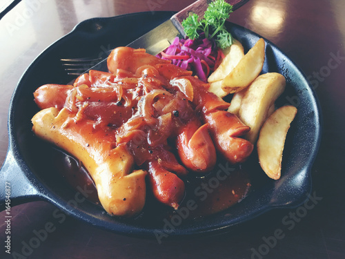 Fried sausages with garlic, herbs and french fries in a pan on the table black Board. still life food. vintage tone. photo