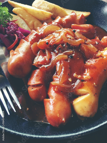 Fried sausages with garlic, herbs and french fries in a pan on the table black Board. still life food. vintage tone. photo