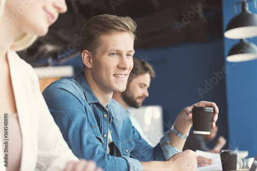 Cheerful youthful guy and other employees doing job in office