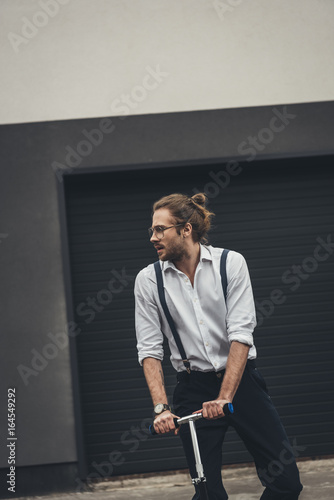 Handsome stylish young man in formal wear and eyeglasses riding scooter and looking away © LIGHTFIELD STUDIOS