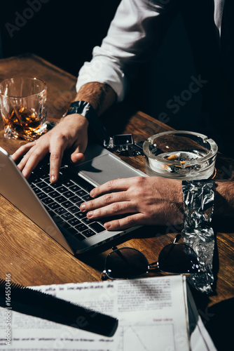 Cropped shot of man with tied hands using laptop at wooden table