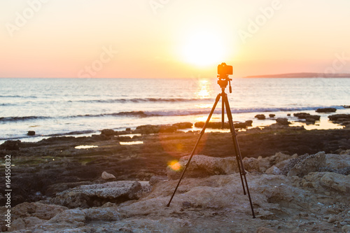 Camera with tripod over sun rising near the beach