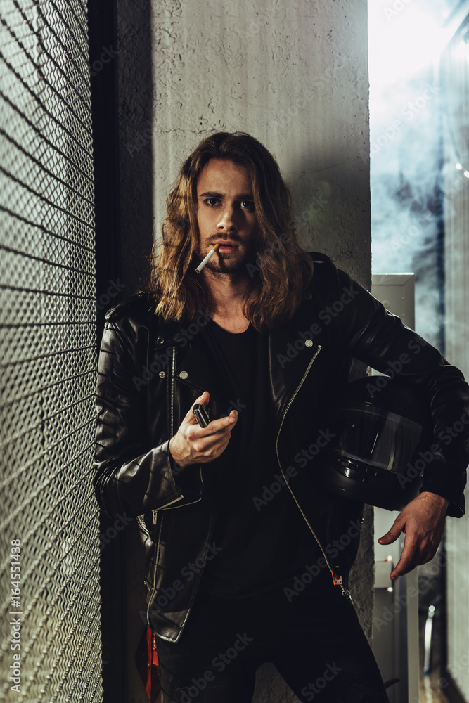 Handsome long haired man in leather jacket holding helmet and lighting  cigarette with lighter Stock Photo | Adobe Stock