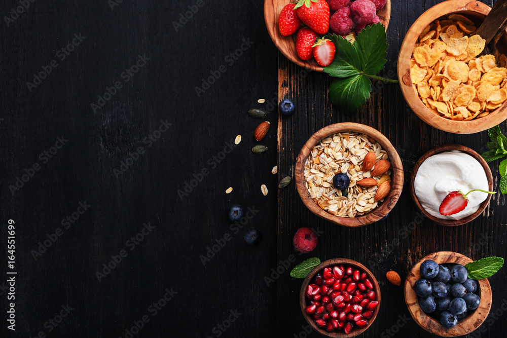 Healthy classic breakfast with oatmeal, cornflakes and various fresh berries on a black wooden surface.