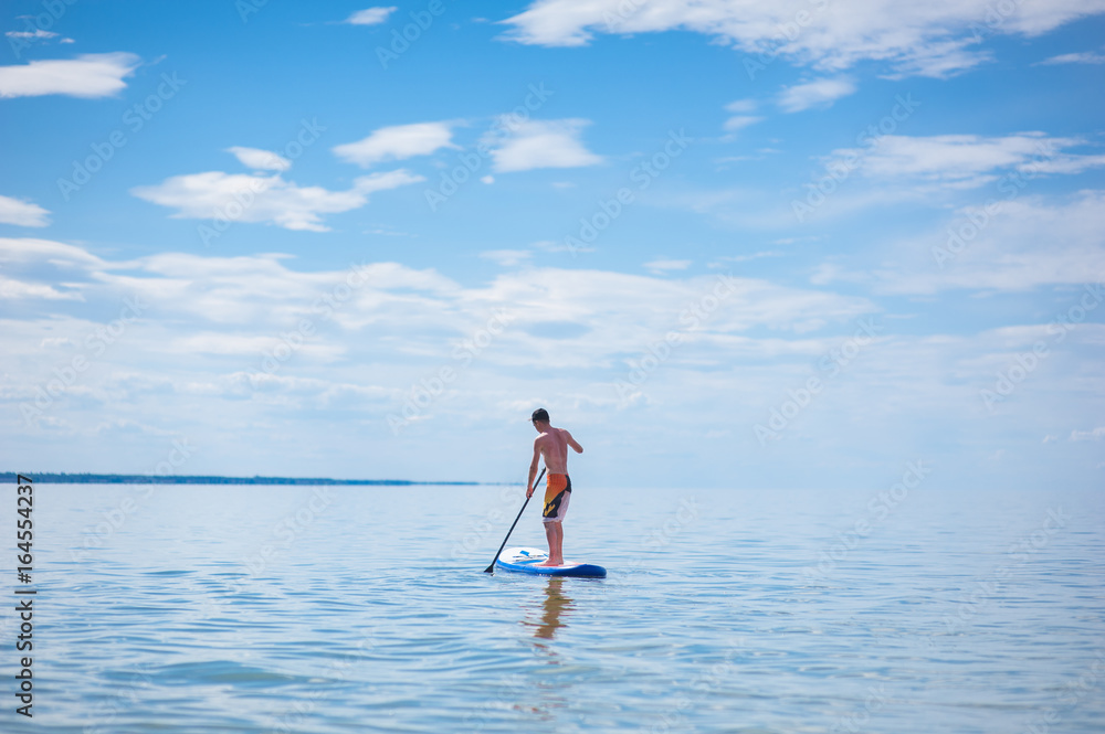 Naklejka premium A young guy is floating on a sup board against the blue sky