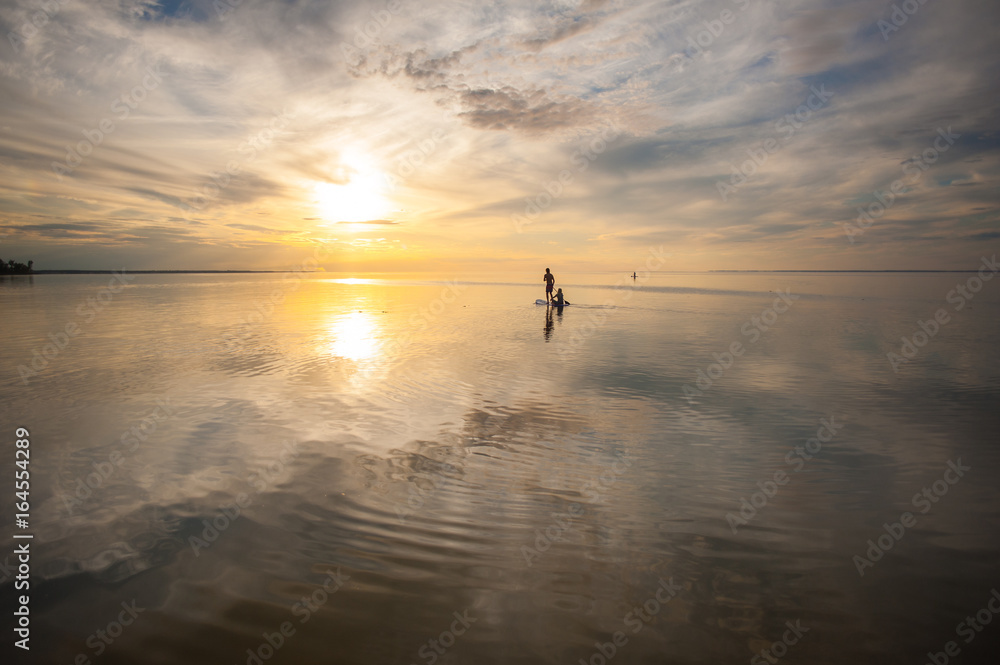 Fototapeta premium A loving couple is swimming on a sup board in the sea or the ocean against a sunset background
