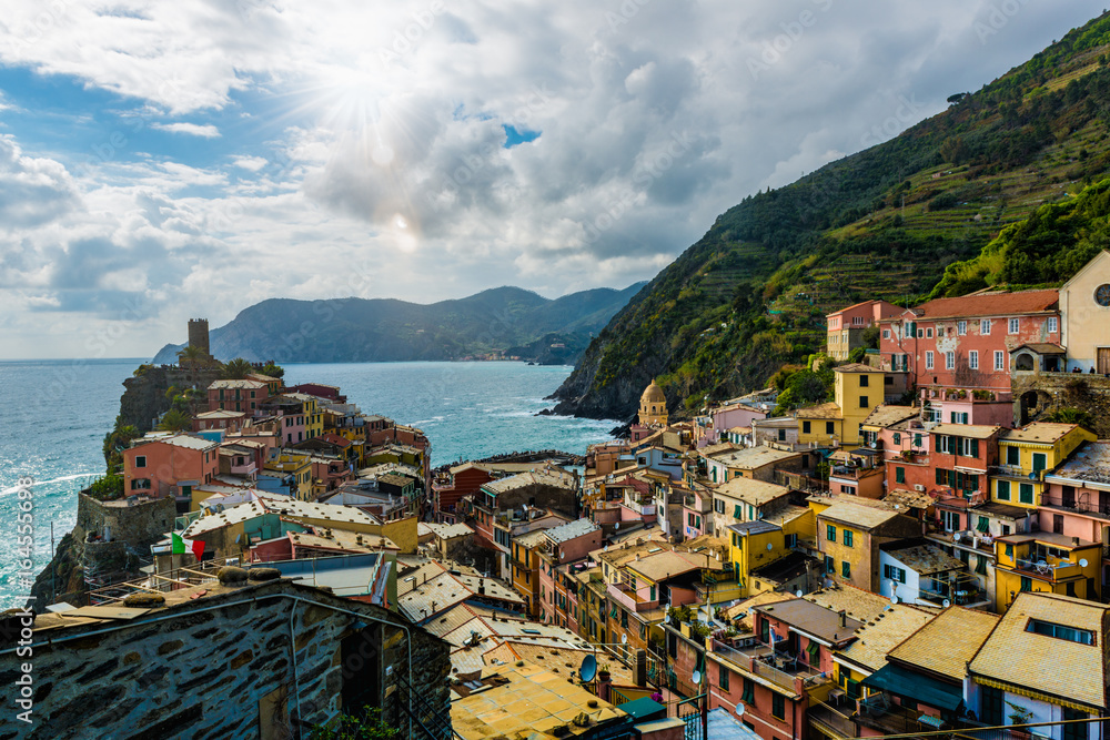 view of famous travel landmark destination Vernazza, a small mediterranean old sea town with harbour coast and castle, Cinque terre National Park, Liguria, Italy. Summer daylight clouds and sun flare