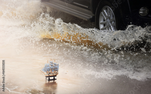 Mini wooden sailboat with motion car runs through flood and water splash during hard rain fall.