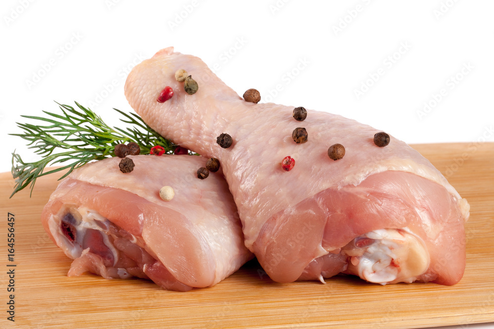 two raw chicken drumsticks on a wooden cutting boardn with a sprig of dill and peppercorns white background two raw chicken drumsticks on a wooden cutting boardn with a sprig of dill and peppercorns white background