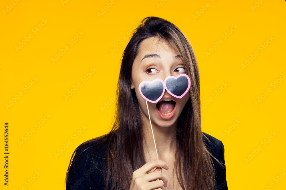 Beautiful young woman on a yellow background holds paper accessories for parties Beautiful young woman on a yellow background holds paper accessories for parties
