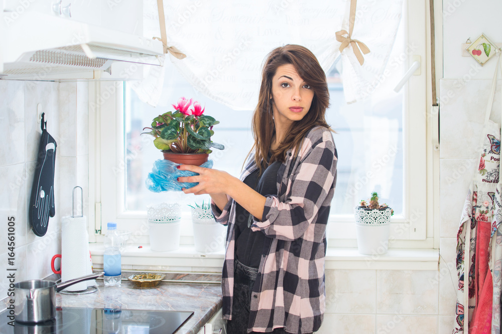 Young woman decorating her kitchen. Portrait of girl holding flower pot indoors. Young woman decorating her kitchen. Portrait of girl holding flower pot indoors.