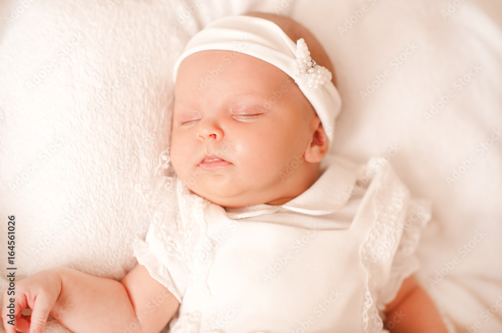 Cute sleeping baby girl wearing white dress and headband in bed close up. Eyes closed. Childhood. Cute sleeping baby girl wearing white dress and headband in bed close up. Eyes closed. Childhood.