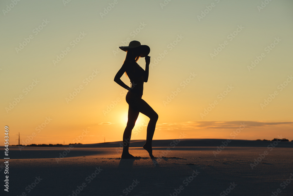 Silhouette of beautiful body woman posing in gold desert at sunset