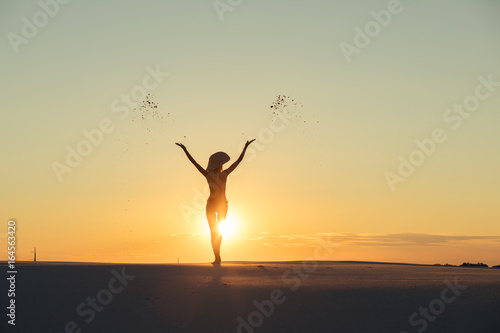 Silhouette of woman throws sand in gold desert at sunset