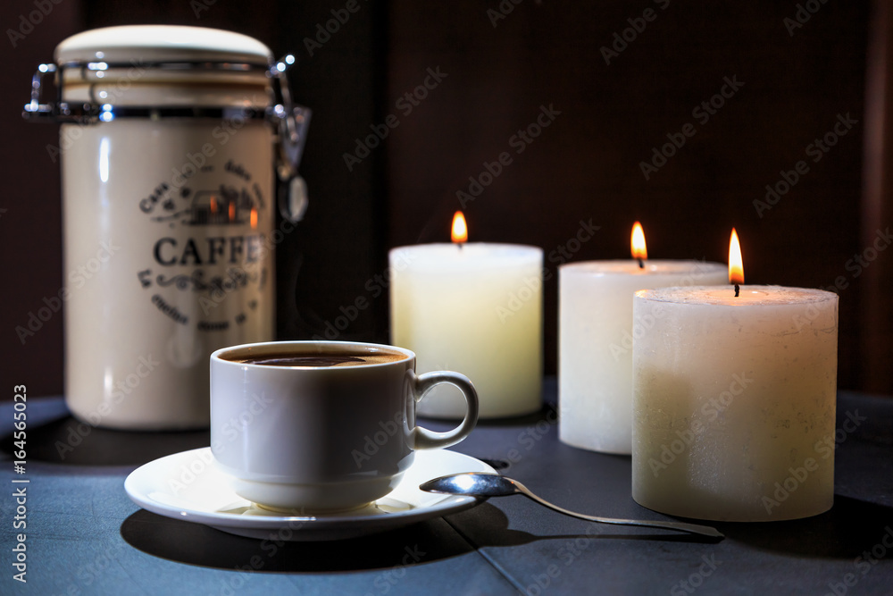 Cup of coffee costs on a table on a background of burning candles Cup of coffee costs on a table on a background of burning candles