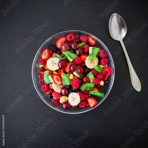 Bowl of healthy fresh fruit salad on dark wooden background. Top view.