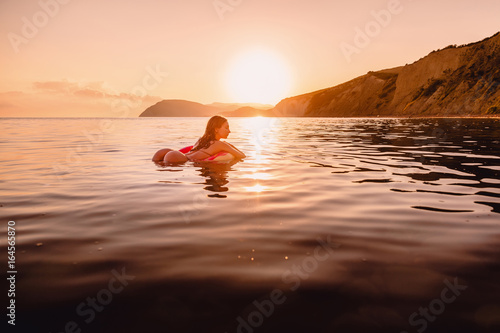 Beautiful woman swimming on the inflatable donut in sea at warm sunset. Slim lady relaxing on her holidays at ocean