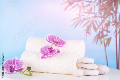 Spa. White towels  stones and orchids lie on the table  against the blue sky.