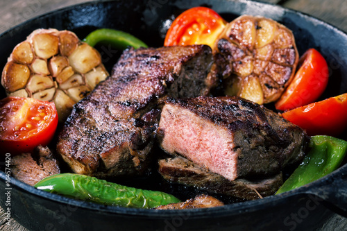 Appetizing beef steak in frying pan with vegetable garnish