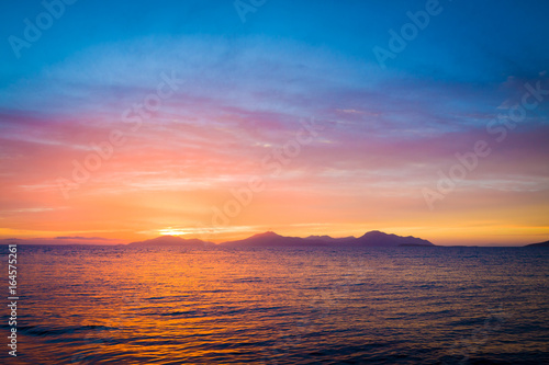 Wonderful sunset behind mountains peak protruding from ocean. © cegli