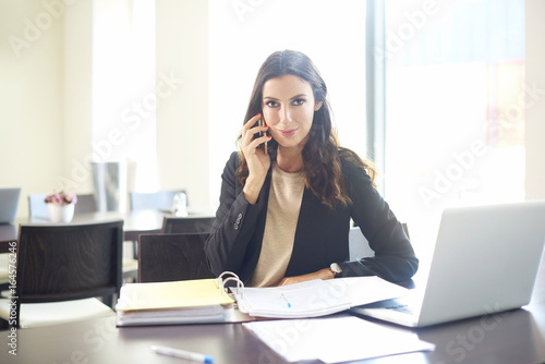Confident young businesswoman portrait. Shot of a young financial professional woman making call and doing some paperwork while sitting at office desk.