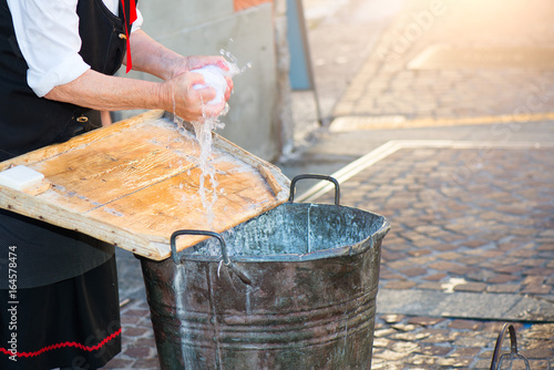 Schilderij op canvas Elderly woman washes the laundry with bucket and wooden board as she once did