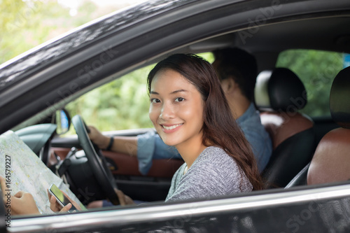 Asian woman using smartphone and map and men driving car on road trip and Happy young couple with a map in the car.
