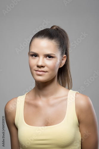 Moody portrait of sporty woman with high pony tail hairstyle looking at camera over gray studio background.