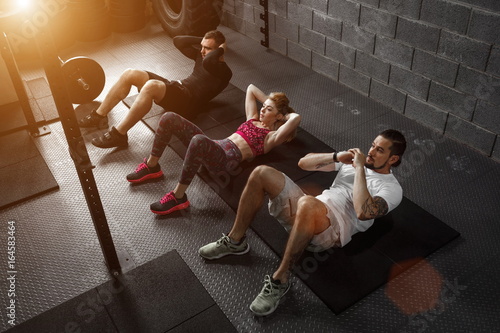 Group of athletic adult men and women performing sit up exercises to strengthen their core abdominal muscles at fitness training photo