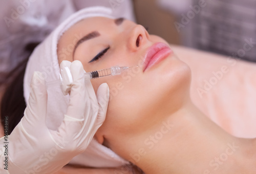 The doctor cosmetologist makes the Botulinotoxin injection procedure for tightening and smoothing wrinkles on the face skin of a beautiful  young woman in a beauty salon.Cosmetology skin care.