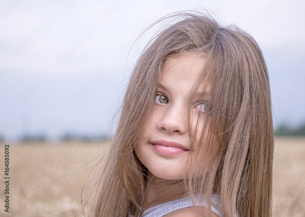 Little girl in golden wheat field in summer day. Portrait of a beautiful child. Concept of purity, growth, happiness