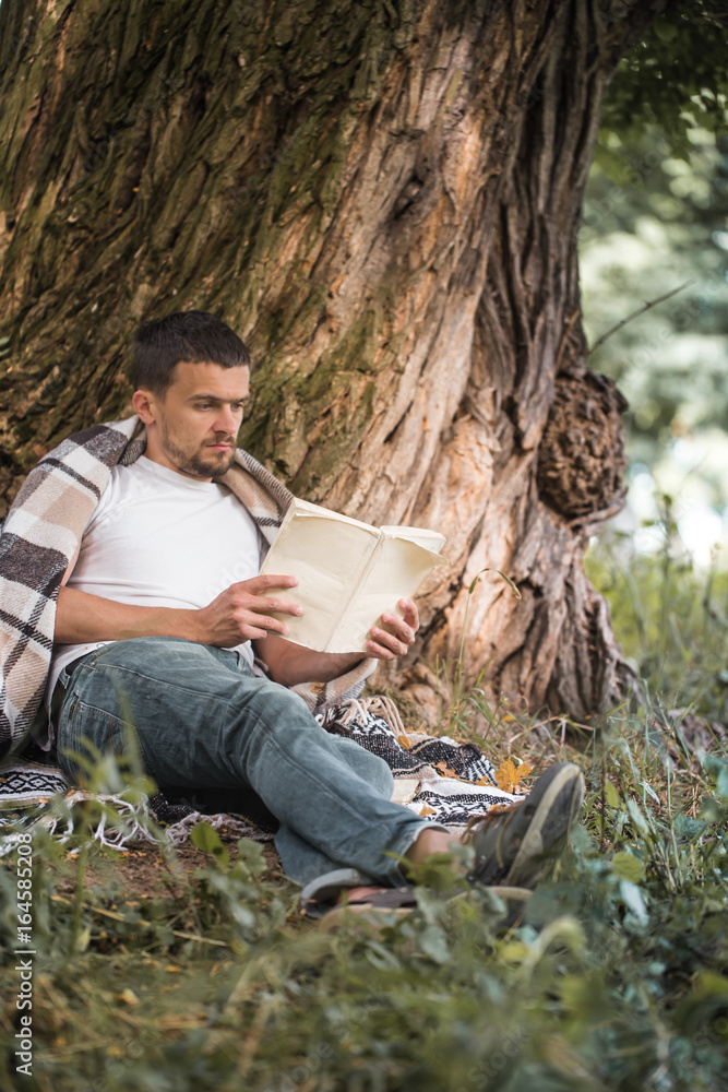 Fototapeta premium The young man at the tree reading a book